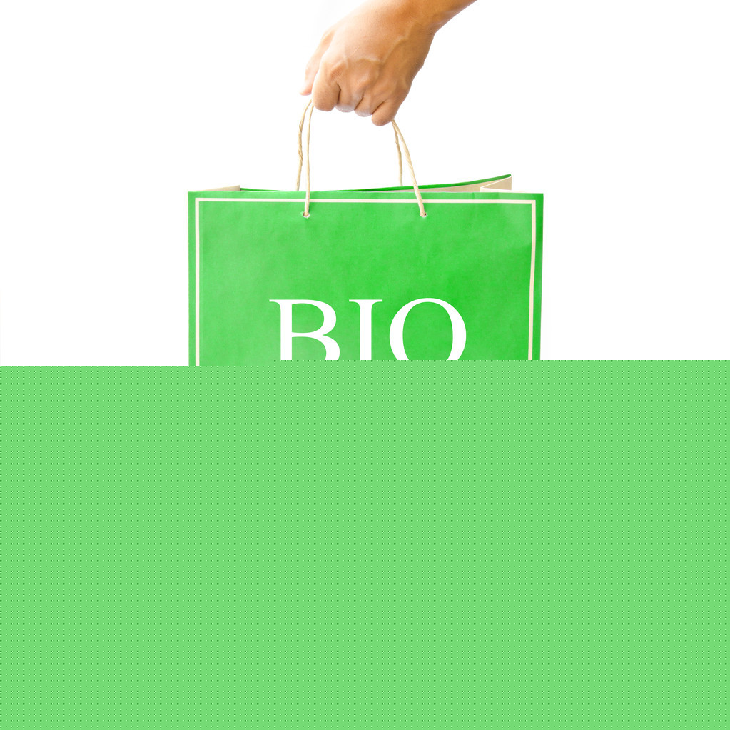 手保持綠色的紙購物袋上反映出白色的地板